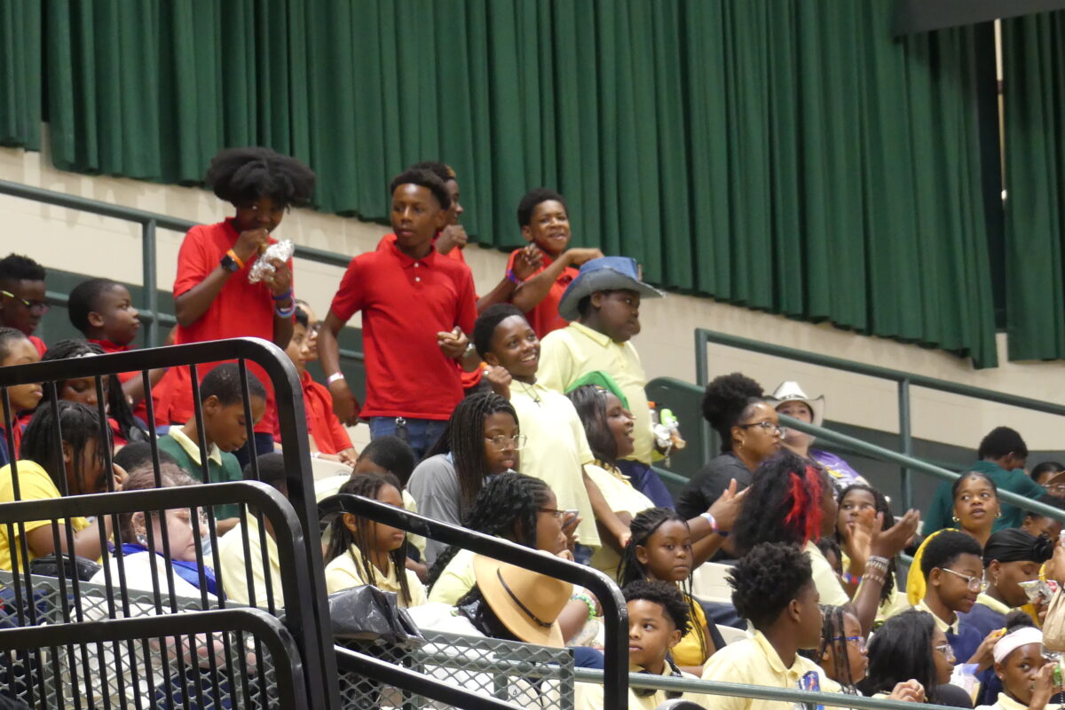A group of young students and spectators watching a live event intently from the stadium bleachers.