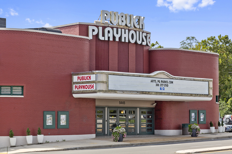 Exterior view of a large, art deco, brick theatre painted red, with a big white marquee sign over the entrance and the words PUBLICK PLAYHOUSE on the top in white letters. The front of the building has rounded corners, curving to the side walls on either side of the marquee.