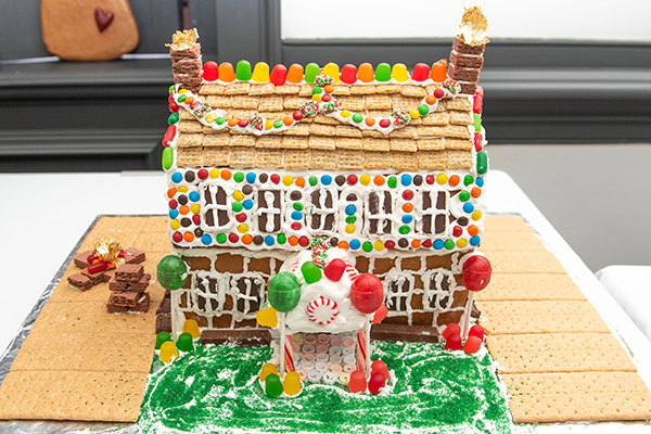A gorgeous two-story gingerbread home with gingerbread and frosting brickwork, and mini wheat shingles. Chocolate candy and gumdrops decorate the exterior of the house. There is a candy cane pillar front entrance, adorned with giant decorative lollipops, and giant graham cracker driveways.