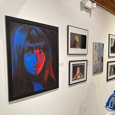 A white wall with various artworks. The most prominent being a painting of a girl with very hard contrasting red and blue lighting.