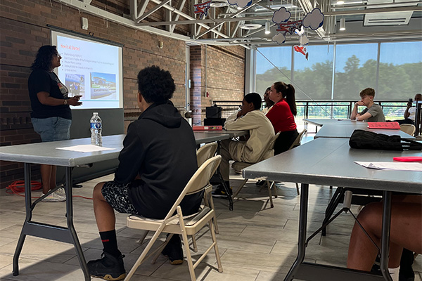 Several teens sitting at tables listening to a lecture about air traffic controllers and their daily jobs and responsibilities.