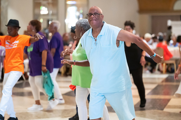 People wearing comfortable clothing, dancing or doing aerobics in formation in a large, multipurpose room.