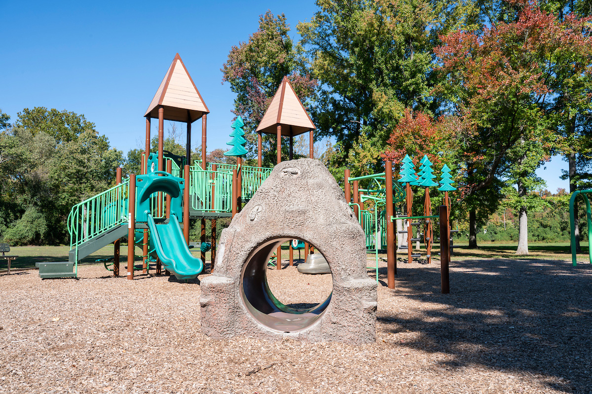 A playground with a large play structure featuring towers, platforms, slides, monkey bars, stairs, fake boulders, and swings.