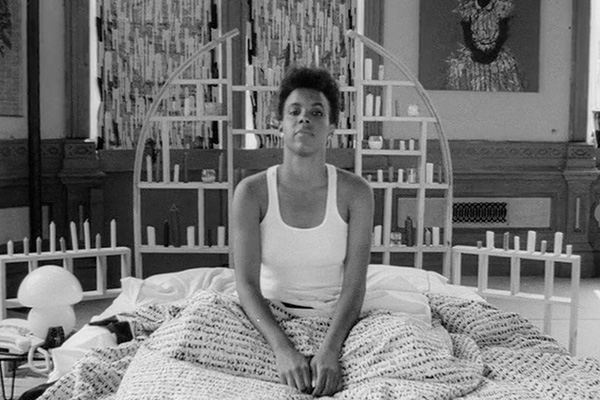 Publicity still from the film She's Gotta Have It depicting a young woman sitting in bed with candles behind her.