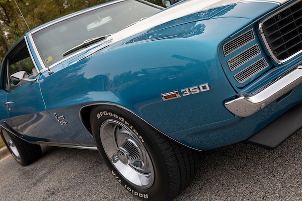 A vintage, blue muscle car with a white stripe down the hood, parked in a parking lot.