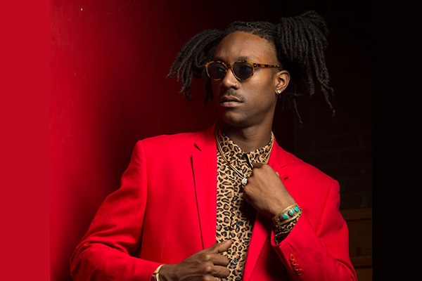 Promotional headshot of a man in a red jacket and leopard-print shirt, wearing sunglasses.