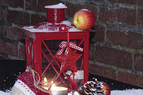 A tea light candle burns inside a red lantern dusted with artificial snow.
